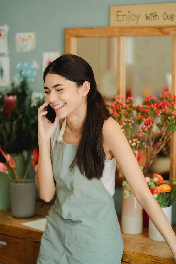 Smiling florist in an apron talking on the phone in a flower shop